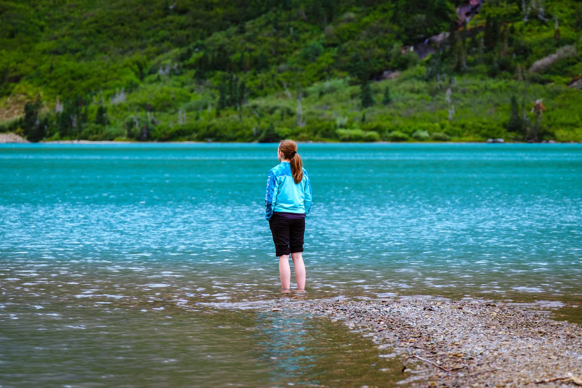 A young adventurer standing at the edge of a turquoise mountain lake.